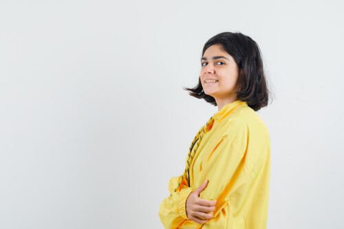 young girl standing straight and looking over shoulder in yellow bomber jacket and looking happy , f